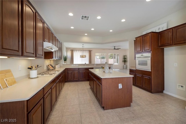 kitchen featuring visible vents, oven, a peninsula, light countertops, and under cabinet range hood