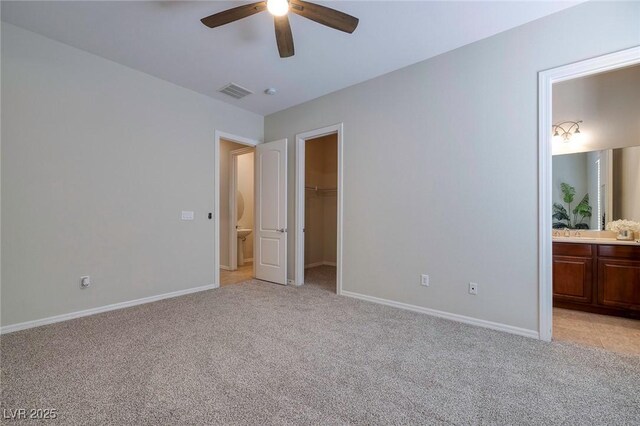 unfurnished bedroom featuring light carpet, a spacious closet, visible vents, and ensuite bathroom