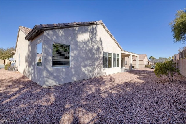 rear view of property featuring a tiled roof, fence, and stucco siding