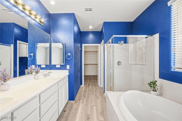 full bath with visible vents, a shower stall, wood finished floors, a bath, and a sink