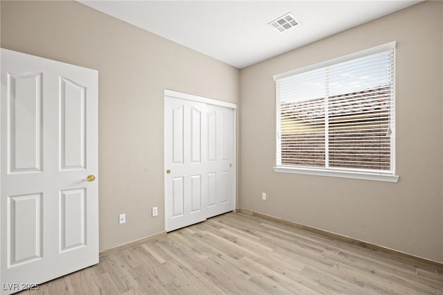 unfurnished bedroom featuring visible vents, light wood-type flooring, a closet, and baseboards