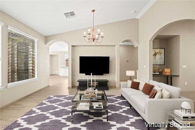 living room featuring visible vents, wood finished floors, arched walkways, an inviting chandelier, and lofted ceiling