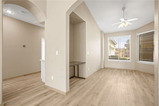 empty room with light wood-type flooring, arched walkways, ceiling fan, and vaulted ceiling