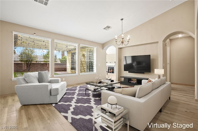 living room featuring arched walkways, visible vents, light wood-type flooring, and a notable chandelier