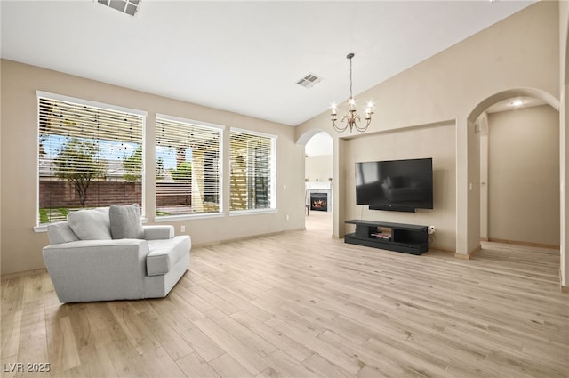 living area with light wood-style floors, visible vents, arched walkways, and a lit fireplace