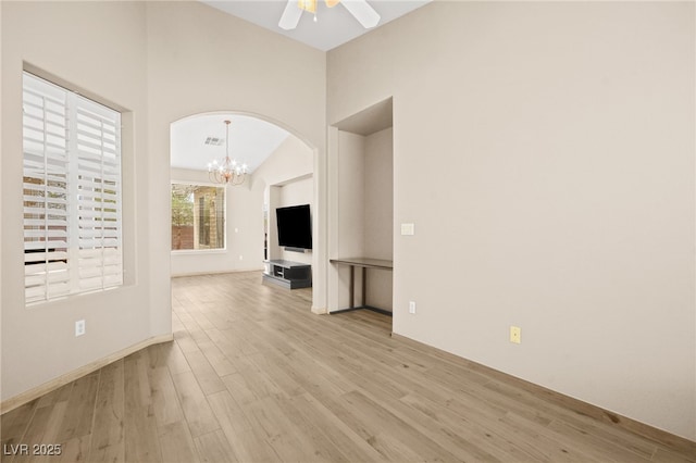 unfurnished living room with visible vents, ceiling fan with notable chandelier, arched walkways, light wood finished floors, and lofted ceiling