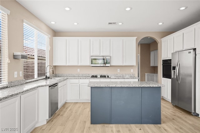 kitchen with visible vents, a kitchen island, appliances with stainless steel finishes, arched walkways, and a sink