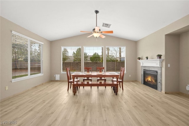 dining space with visible vents, ceiling fan, a tiled fireplace, light wood-type flooring, and lofted ceiling