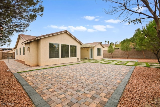 rear view of property featuring stucco siding, a patio, a fenced backyard, and a tile roof