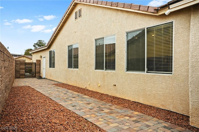 view of side of property featuring a patio area, stucco siding, a tiled roof, and fence