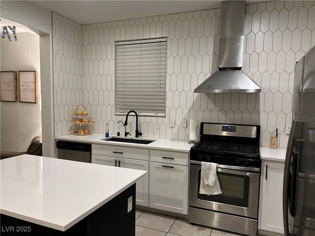 kitchen featuring light countertops, appliances with stainless steel finishes, light tile patterned flooring, wall chimney exhaust hood, and a sink