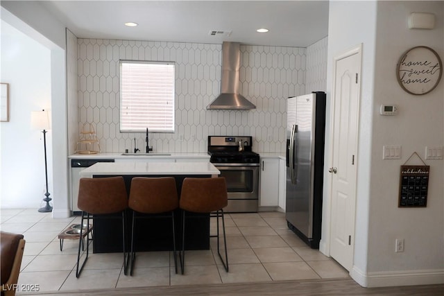 kitchen with a sink, decorative backsplash, light countertops, stainless steel appliances, and wall chimney exhaust hood