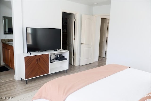 bedroom with ensuite bath and light wood-style floors