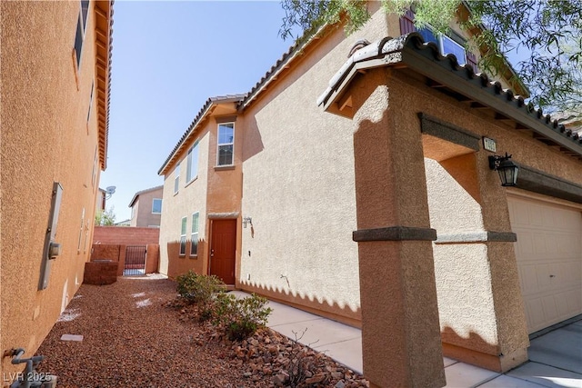 view of side of property with a garage, stucco siding, and fence