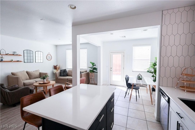 kitchen featuring light countertops, a breakfast bar, open floor plan, stainless steel dishwasher, and light tile patterned floors