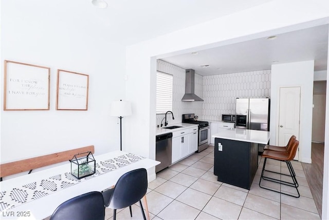 kitchen featuring light countertops, appliances with stainless steel finishes, a breakfast bar area, wall chimney range hood, and a center island