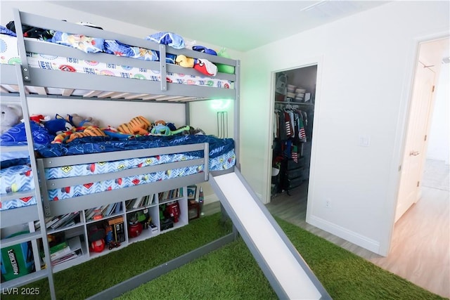 bedroom with a walk in closet, baseboards, a closet, and wood finished floors