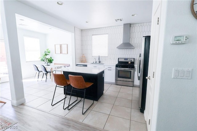 kitchen with wall chimney range hood, a sink, appliances with stainless steel finishes, and a wealth of natural light