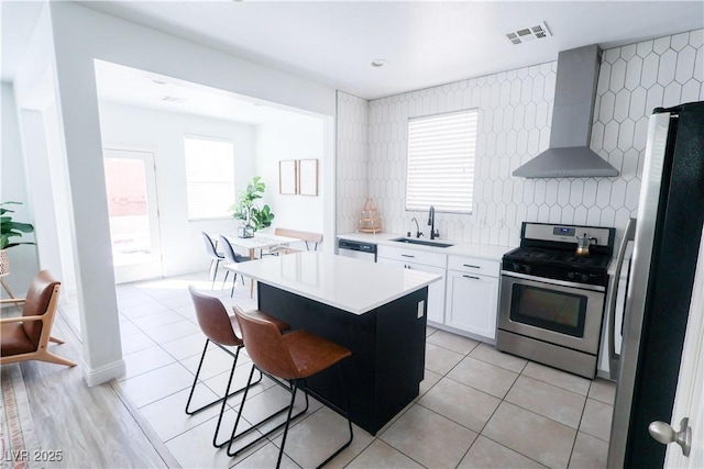 kitchen featuring a kitchen breakfast bar, stainless steel appliances, a sink, visible vents, and wall chimney range hood