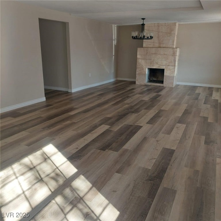 unfurnished living room with baseboards, an inviting chandelier, wood finished floors, and a tile fireplace