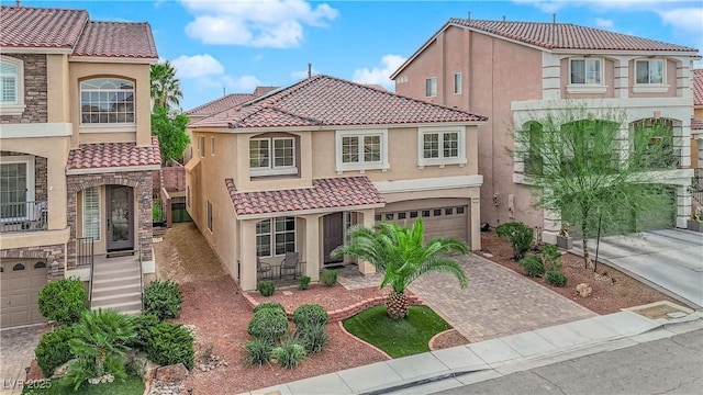 mediterranean / spanish house featuring a garage, a tile roof, decorative driveway, and stucco siding