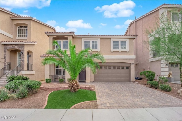 mediterranean / spanish-style home featuring decorative driveway, a tiled roof, an attached garage, and stucco siding