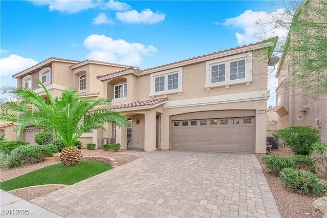 mediterranean / spanish house with a garage, a tiled roof, decorative driveway, and stucco siding