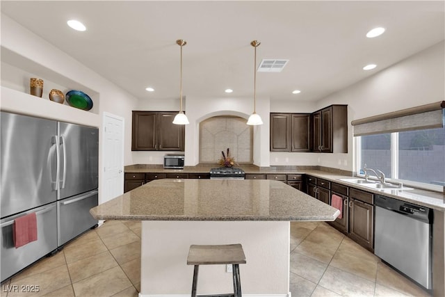 kitchen featuring a center island, visible vents, appliances with stainless steel finishes, dark brown cabinets, and light stone countertops