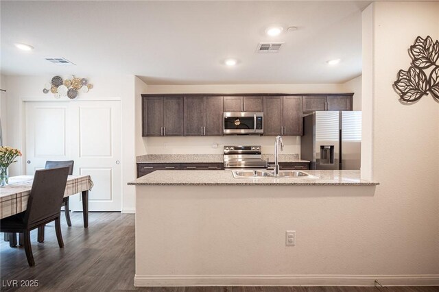 kitchen featuring dark brown cabinetry, stainless steel appliances, a sink, visible vents, and dark wood-style floors