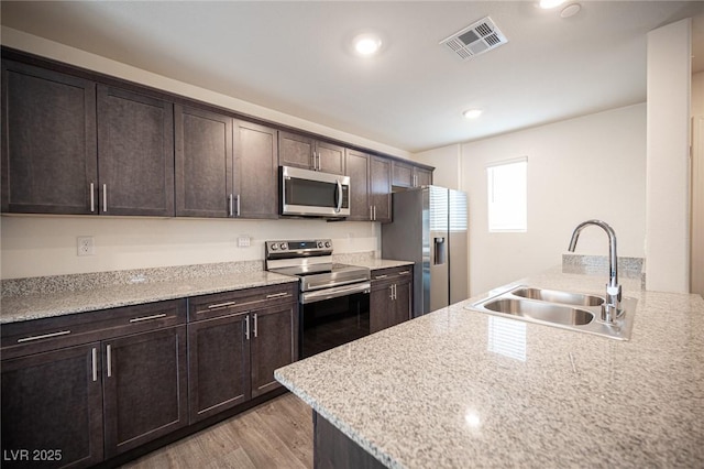 kitchen featuring dark brown cabinetry, visible vents, appliances with stainless steel finishes, light wood-type flooring, and a sink