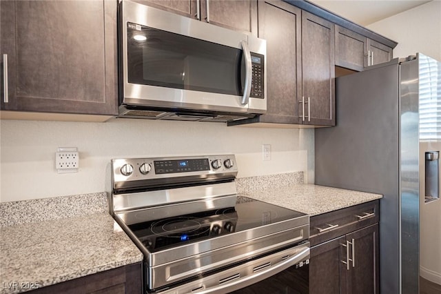 kitchen featuring stainless steel appliances, dark brown cabinets, and light stone countertops