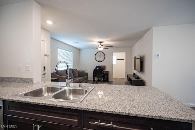 kitchen with light stone countertops, a ceiling fan, open floor plan, and a sink