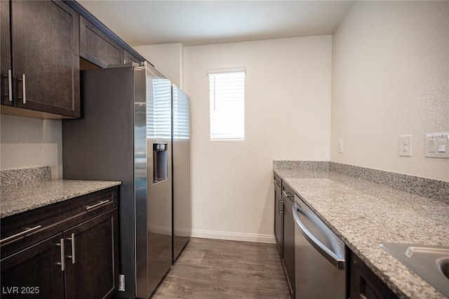 kitchen featuring dark brown cabinetry, baseboards, light stone counters, dark wood-style flooring, and stainless steel appliances