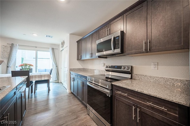 kitchen featuring dark brown cabinetry, light wood finished floors, visible vents, light stone counters, and stainless steel appliances