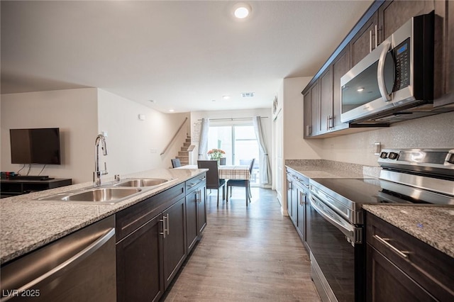 kitchen with light wood-type flooring, appliances with stainless steel finishes, dark brown cabinets, and a sink