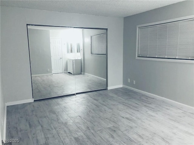 unfurnished bedroom featuring a textured ceiling, baseboards, and wood finished floors