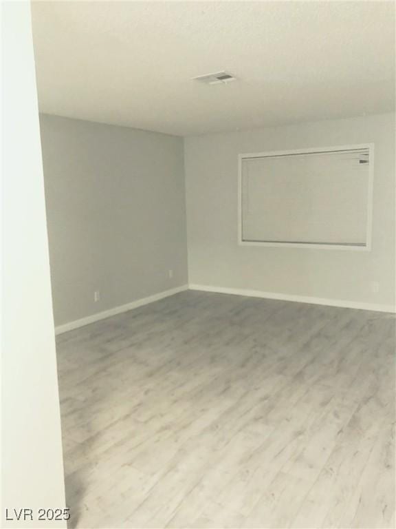 spare room with wood finished floors, visible vents, and baseboards