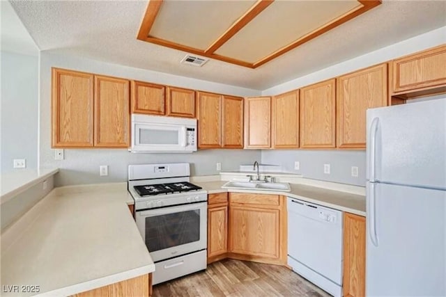 kitchen with white appliances, light wood finished floors, visible vents, light countertops, and a sink