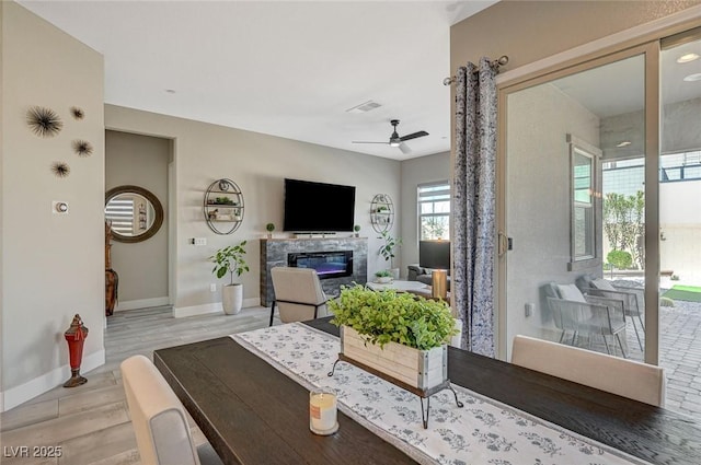 living area with baseboards, visible vents, a ceiling fan, a glass covered fireplace, and light wood-style flooring