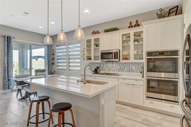 kitchen featuring tasteful backsplash, white cabinets, appliances with stainless steel finishes, light countertops, and a sink