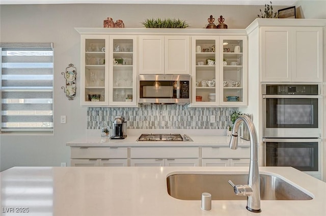 kitchen with tasteful backsplash, stainless steel appliances, light countertops, white cabinetry, and a sink