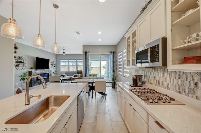 kitchen featuring stainless steel appliances, a sink, visible vents, backsplash, and decorative light fixtures