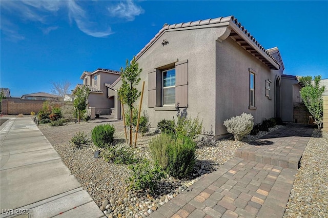 view of property exterior with a patio area, a tile roof, fence, and stucco siding