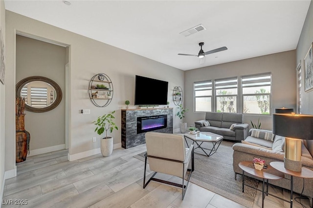 living area featuring baseboards, visible vents, ceiling fan, light wood-style flooring, and a fireplace