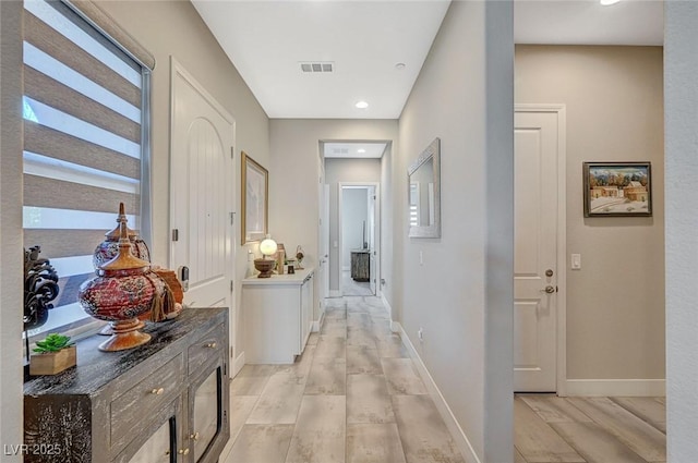 hallway featuring light wood-style floors, visible vents, and baseboards