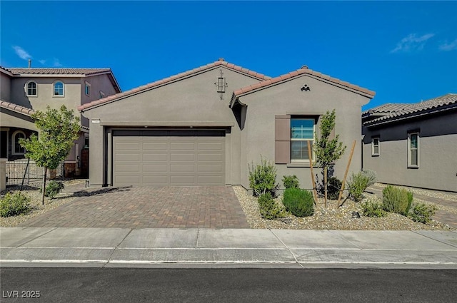 mediterranean / spanish-style home featuring a garage, a tiled roof, decorative driveway, and stucco siding