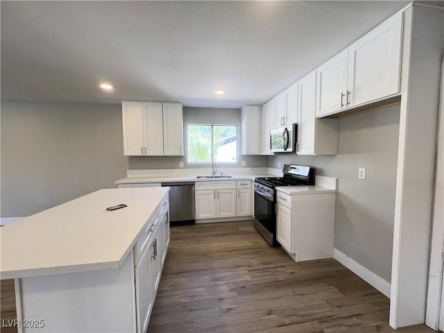 kitchen with stainless steel appliances, dark wood-type flooring, white cabinetry, a sink, and baseboards