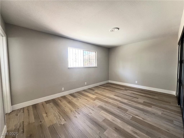 spare room with a textured ceiling, baseboards, and wood finished floors