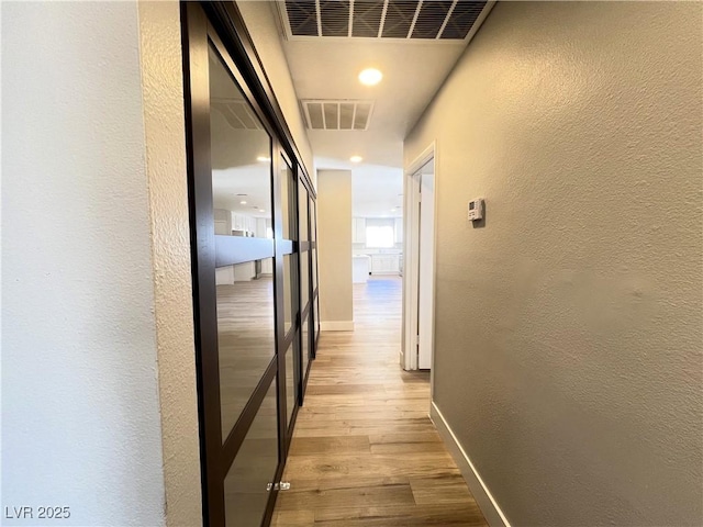 hall with visible vents, a textured wall, baseboards, and wood finished floors