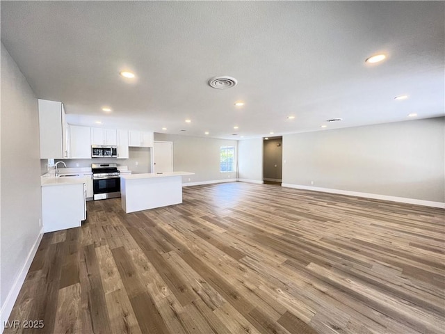 kitchen featuring white cabinets, open floor plan, wood finished floors, stainless steel appliances, and a sink